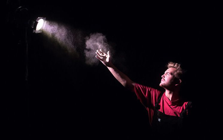 Drama student dramatically shot against background reaching up to single spotlight
